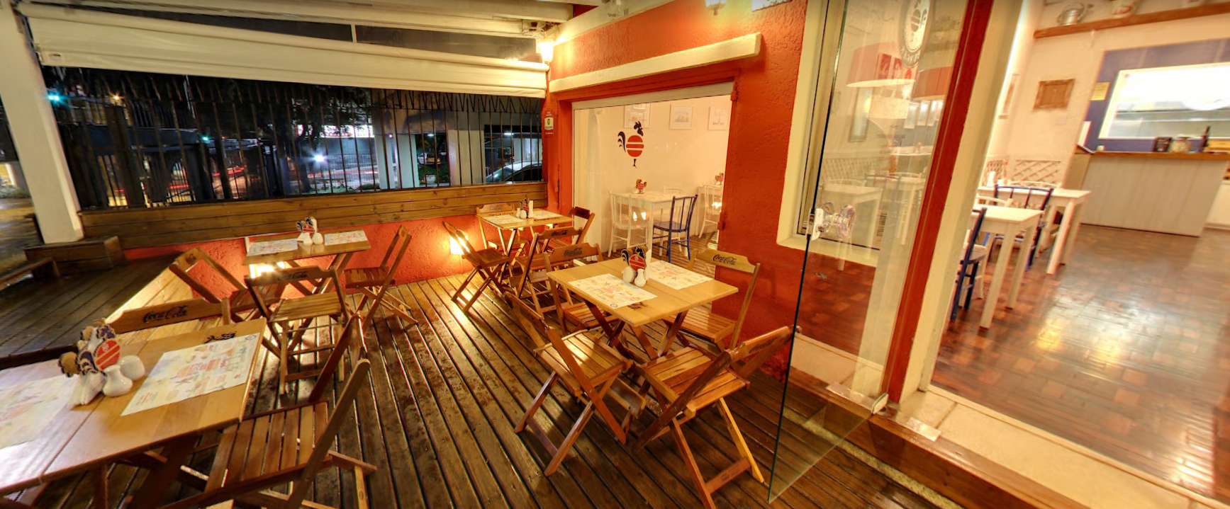 Deck externo de madeira com mesinhas e o galo da casa na parede