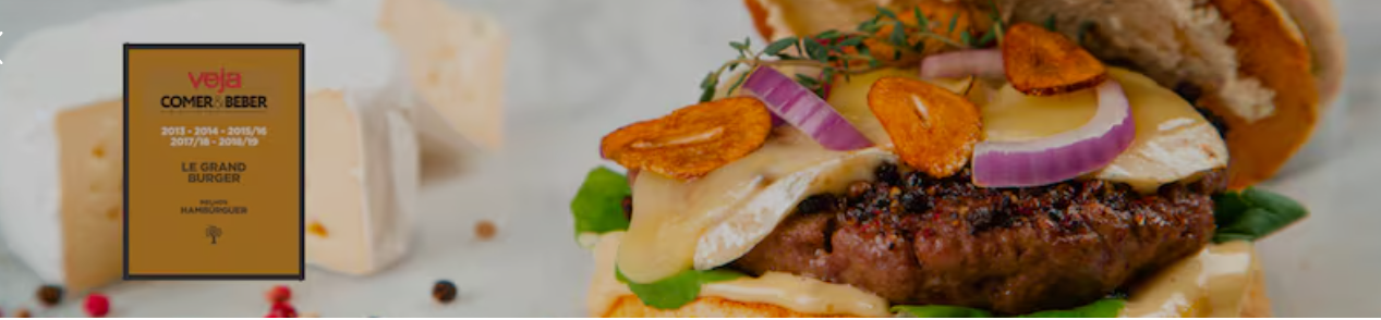 Hambúrguer com camembert, cebola roxa e chips de alho crocante, ao lado da placa de premiação da casa